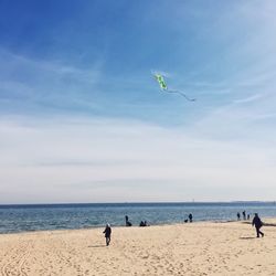 Low angle view of kite over people at beach against sky on sunny day