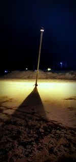 Illuminated street light on beach against sky at night