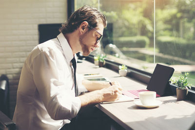 Businessman writing in book while sitting at desk in office