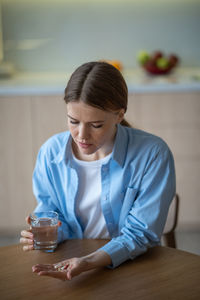 Stressed unhealthy woman holding capsules, glass of water, suffering from chronic pain, disease