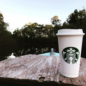 Coffee cup on table by lake against sky