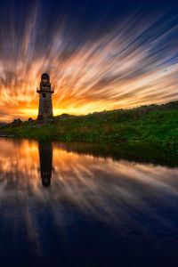 Lighthouse by building against sky during sunset