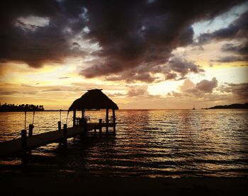 Silhouette wooden posts in sea against sky at sunset