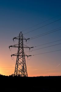 Low angle view of silhouette electricity pylon on field against sky during sunset