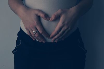 Midsection of pregnant woman standing against wall