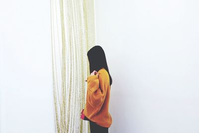 Side view of woman standing by decoration hanging against white wall