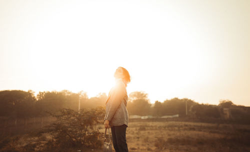 Rear view of woman standing against sky during sunset