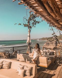 Woman sitting on chair by sea against sky