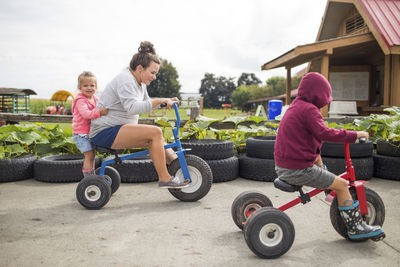 Mother biking on tricycles with her two kids outdoors.