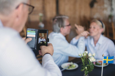 Senior man photographing couple having drinks in restaurant