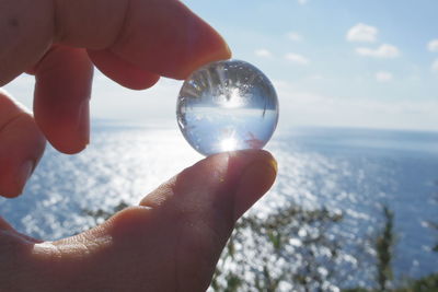 Close-up of cropped hand holding crystal sphere by sea