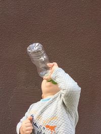 Little boy drinking water from a plastic bottle near a brown stone wall