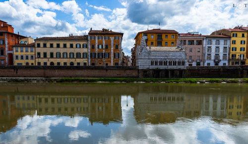 Arch bridge over river by buildings against sky