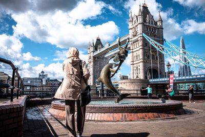 Rear view of woman watching girl and dolphin statue by london bridge