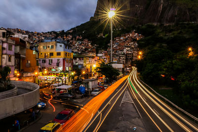 Light trails on road amidst buildings against sky at night