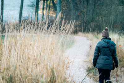 Rear view of woman walking amidst grass against trees