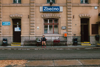 Woman sitting on bench against building in city