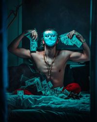 Young man wearing mask while sitting with money and guitar on bed