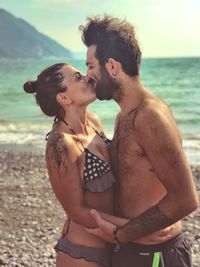 Side view of couple kissing while standing at beach