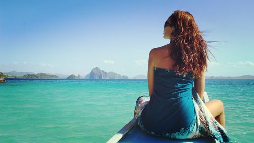 Rare view of young woman sitting on wooden structure on sea against sky