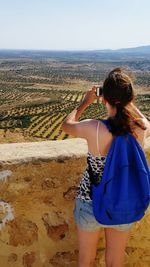 Rear view of young woman photographing olive tree farm