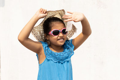 An indian girl wearing sunglasses and holding hat looking at the sun in summer on white background