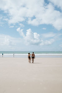 Rear view of people at beach against sky