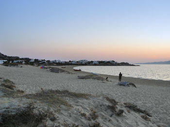 People on beach against clear sky during sunset