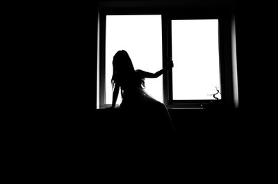 Silhouette woman standing by window in darkroom