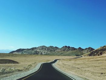 Empty road leading towards mountains against clear blue sky
