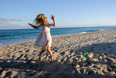 Rear view of woman standing at beach against sky