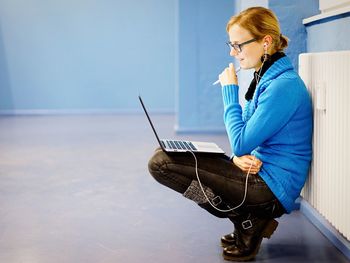 Side view of woman sitting on floor with laptop