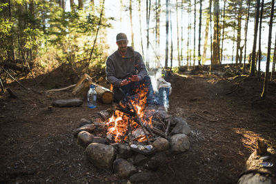 Man warming by the fire at sunset while car camping in coastal maine