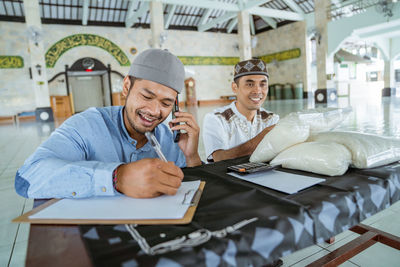 Smiling man writing while talking on phone at mosque