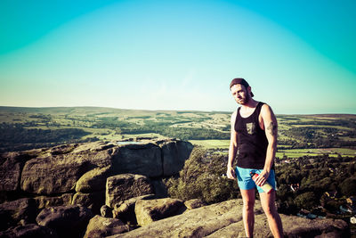 Portrait of man standing on rock against sky