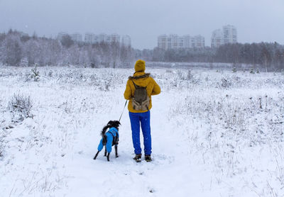 Young woman with fluffy dog from the back on snow. walking with pet 