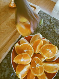 Cropped hand having oranges in bowl on table