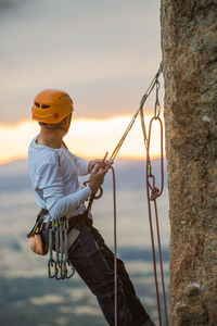 Side view of sportive male alpinist ascending on cliff in mountain terrain in cloudy day