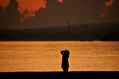 Rear view of silhouette woman standing at beach during sunset