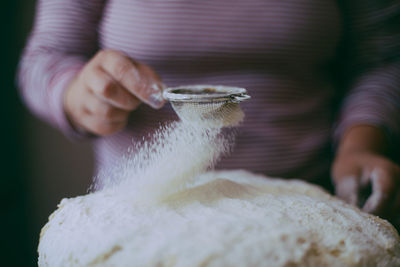Midsection of woman sieving flour in kitchen