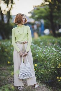 Woman holding bag while standing by plants