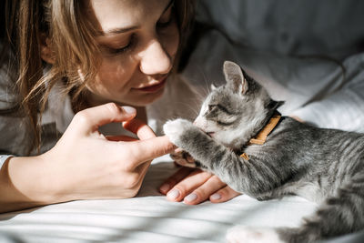 Candid portrait of young woman is resting with kitten on the bed at home one sunny day. girl play