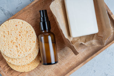 Top view amber glass cream bottle, homemade soap, face sponges on wooden board. spa 