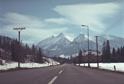 Empty road leading towards mountains against sky during winter
