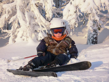 Boy wearing ski fallen against trees on snow covered field
