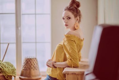 Young woman looking away while sitting on table at home