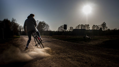 Rear view of man riding bicycle on dirt road