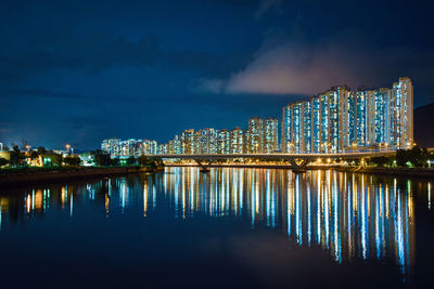 Illuminated buildings by lake against sky in city at night