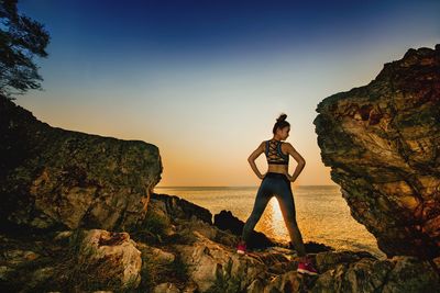 Rear view of woman standing by sea on rock during sunset