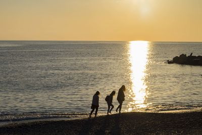 Silhouette people standing at beach during sunset